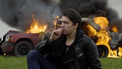 Man smokes against the background of a burning car, despair, a fire, an Stock Footage 95201293