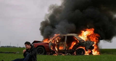 Man smokes against the background of a burning car, despair, a fire, an Stock Footage 95203025