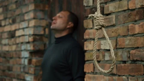 A man smokes against the background of a rope with a noose for suicide. Video stock 343734360