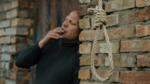 A man smokes against the background of a rope with a noose for suicide. Stock Footage 343734368