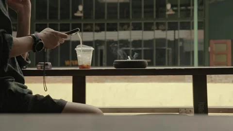Man smokes cigarette drinks coffee use mobile phone on wooden table by street Stock-Footage 278547653