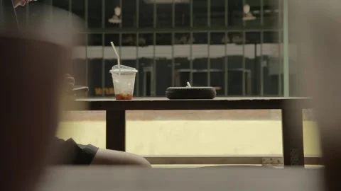 Man smokes cigarette drinks coffee use mobile phone on wooden table by street Stock Footage 278547710