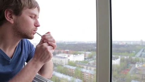 Man smokes a cigarette at the open window. High floor. Natural light Stock Footage 76116362