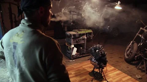Man smokes a cigarette, tuning in to work in the garage. 库存影片 61485149