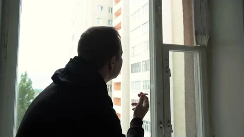 Man smokes a cigarette while sitting on the windowsill Stock Footage 164613897