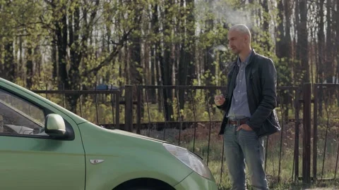 A man smokes a cigarette while standing near a green passenger car Stock Footage 153922667