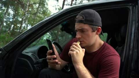 Man smokes electronic cigarettes while sitting in the car and uses the phone Stock Footage 159707455