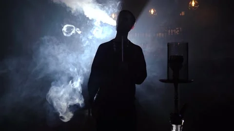 Man smokes hookah at bar in dark on background blue light. Night bar with hookah Stock Footage 149240692