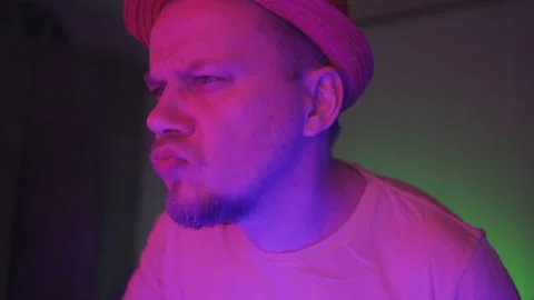 A man smokes a hookah while sitting in the neon lighting of the room and listens Stock Footage 130600348