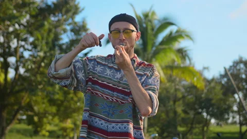 Man smokes marijuana from pipe, blowing smoke into camera Stock Footage 233607909