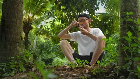 Man smokes marijuana from pipe relaxing alone in park. Person smoking cannabis Stock Footage 233897948