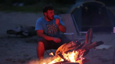 The man smokes a pipe while sitting by the fire at night Stock Footage