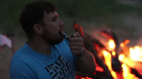 The man smokes a pipe while sitting by the fire at night Stock Footage