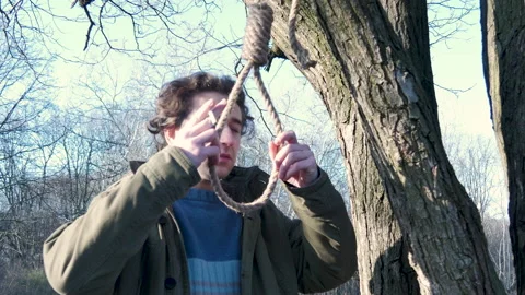 Man smokes, thinks of hanging himself on rope. Trying to commit suicide in park Stock Footage 149326228