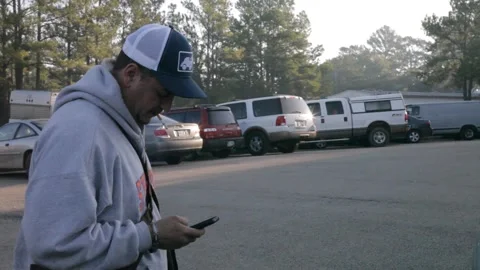 Man Smoking Cigarette and Using Smartphone in Parking Lot Stock Footage 345274941