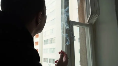 Man smoking a cigarette sitting by the window 4k footage Vídeo Stock 162039573