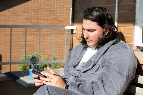 Man smoking cigarette using smartphone on balcony Stock Photos