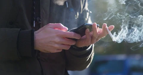 Man is smoking cigarette while browsing on a mobile phone 스톡 동영상 104978306