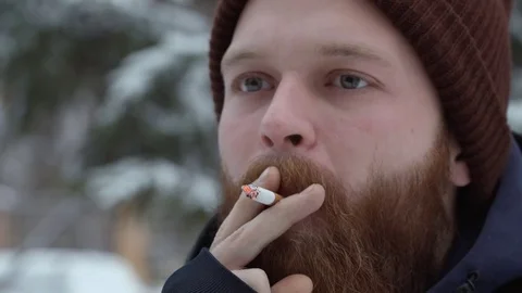 Man smoking cigarette, young bearded hipster in hat and jacket at forest on Stock-Footage 84686702