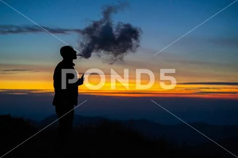 The man smoking an electronic cigarette on the sunset background Stock Photos