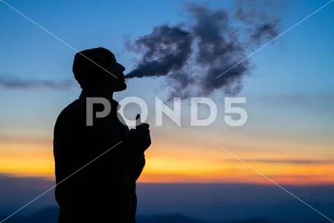 The man smoking an electronic cigarette on the sunset background Stock Photos