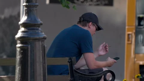 A man smoking a small cigar while using his phone on a street bench Video stock 281067527