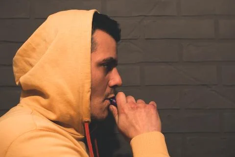 Man is smoking Vape Pod System at home near the gray wall. Electronic cigar.. Stock Photos