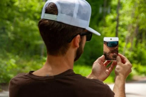 A man smoking while his reflection is seen in a small pocket mirror outdoors Stock Photos