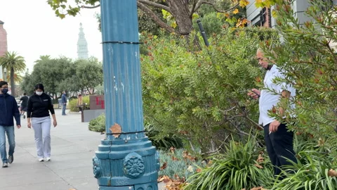 Man smoking while people walking pass by wearing masks in San Francisco Видео 144294911