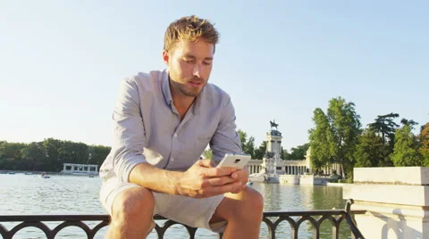 Man sms texting using app on smart phone at sunset in city park Stock Footage 62736923