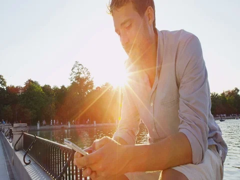 Man sms texting using app on smart phone at sunset in city park Stock Footage 75556360