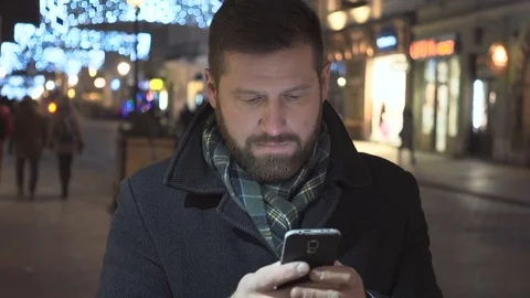 Man sms typing on smartphone app, smiling at camera, night, steadycam Vídeos de archivo 72782000