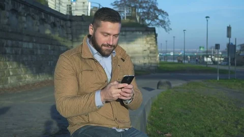 Man sms typing using app on smart phone sitting on wall at boulevard  库存影片 72775198