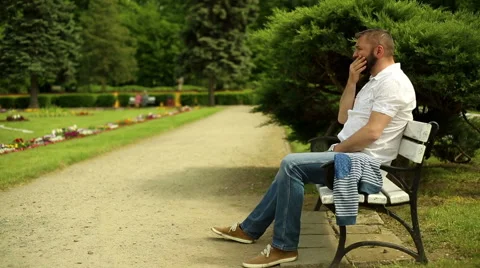 Man sneeze, sitting on a bench at the park Stock Footage 64284048