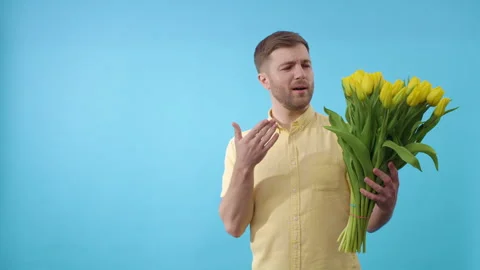 Man sneezes while holding yellow tulips on blue background Stock Footage 279466496