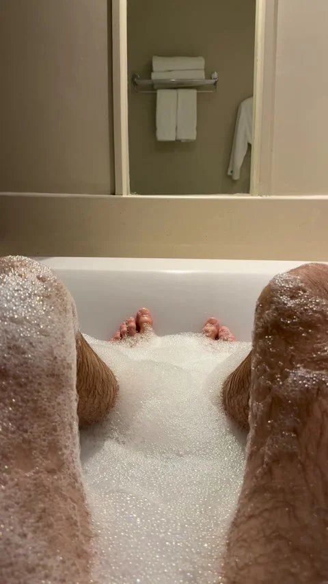 Man soaking in a bubble bath, with foam-covered legs and feet visible in a Stock Footage 345636423