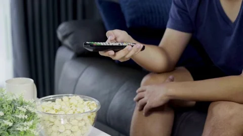 Man on sofa flipping through television channels with remote control in hand. Stock Footage 257873908