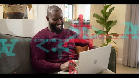 Man on sofa joining call on laptop for work, typing, waving while teal-red code Stock Footage 332639665