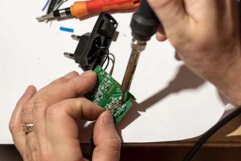 A man solders wiring in the electronic circuit board of the device Stock Photos