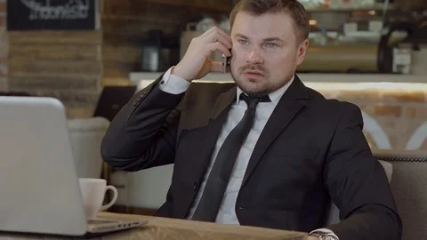 Man solves business issues in cafe on the phone sitting in front of laptop Stock Footage 70593201