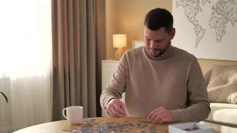 Man solving puzzle at wooden table indoors, camera moving right Stock Footage 305020568