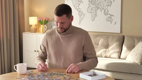 Man solving puzzle at wooden table indoors, camera moving left Stock Footage 305108515