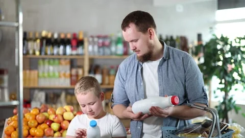 Man with son hold packages bottles and choose consider milk in store Stock Footage 313459516