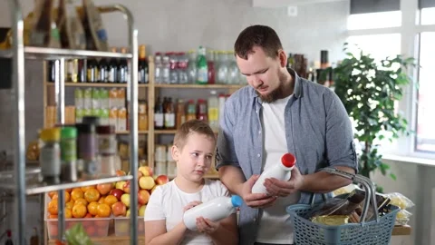 Man with son hold packages bottles and choose consider milk in store Stock Footage 326317428