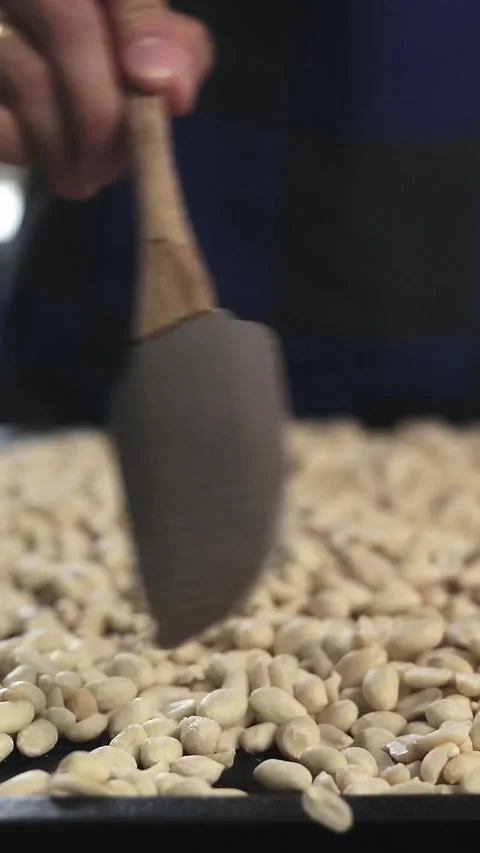 Man sorting raw peanuts with a rubber spatula in a rustic setting for roastin Stock Footage 305855462