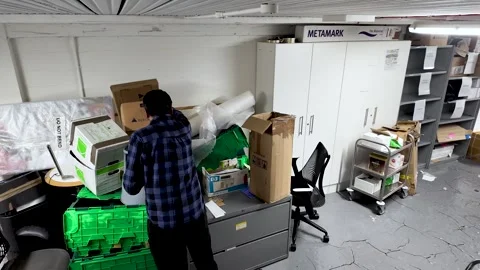 A man is sorting through cardboard boxes and clutter in a basement office He is 動画素材 327788142