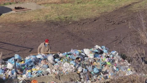 A man sorts garbage at a landfill, scooping up waste, plastic products and bags. Stock Footage 252439523