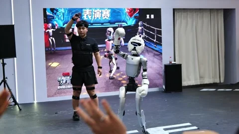 A man in a sparring stance faces a boxing humanoid robot. Stock Footage 344272821