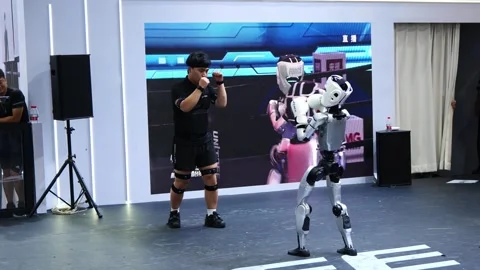 A man in a sparring stance faces a boxing humanoid robot. Stock Footage 344272822