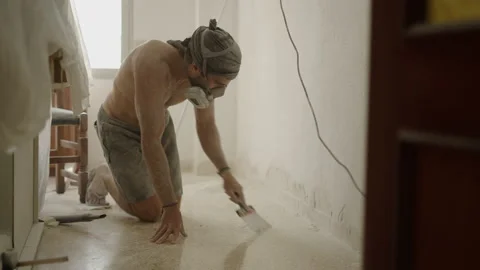 Man with spatula removing the dust from the floor, standing on his knees Video stock 209601474